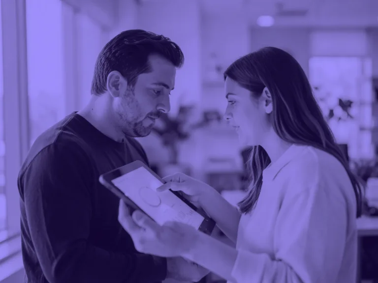 Un hombre y una mujer de pie revisan juntos unas gráficas en una tableta en una oficina luminosa
