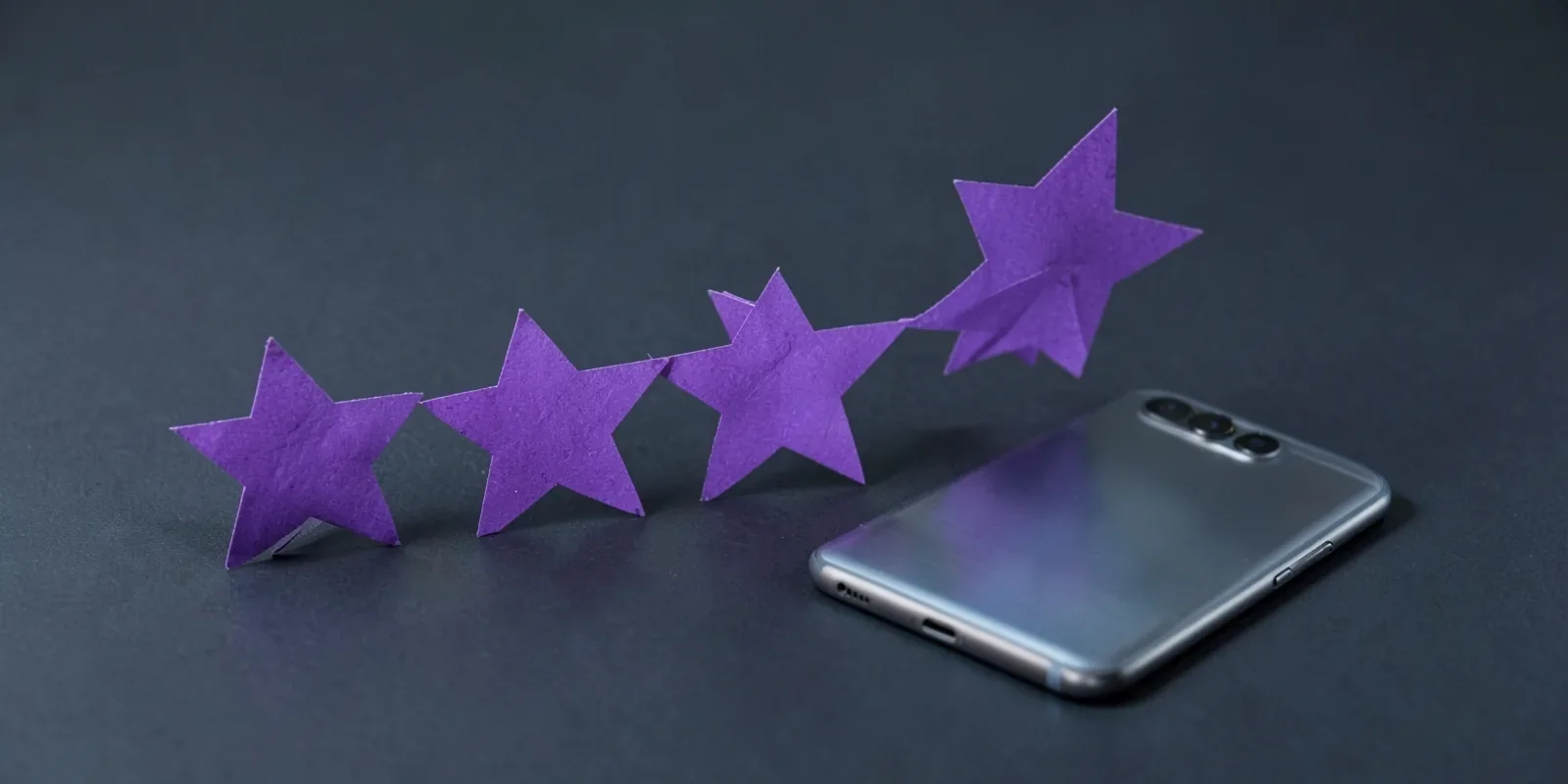 Cinco estrellas de papel violeta en fila junto a un móvil boca abajo, la idea de sumar reseñas en Google