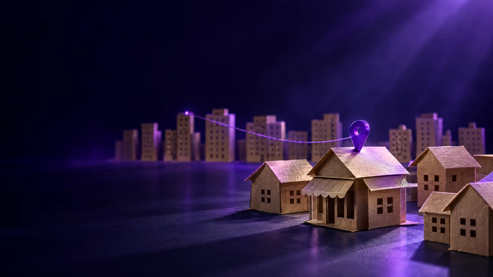 Casitas de papel de un pueblo con una chincheta violeta en una tienda, unida por un hilo a una ciudad de cartón