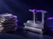 Pila de fotografías impresas junto a una prensa de tornillo con manivela violeta que aplasta otra pila hasta dejarla fina