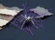 Araña metálica en miniatura sobre una telaraña de hilo violeta tendida entre trozos de papel crudo