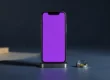 Teléfono móvil de pie sobre una peana metálica con la pantalla violeta, junto a un pequeño nivel de burbuja