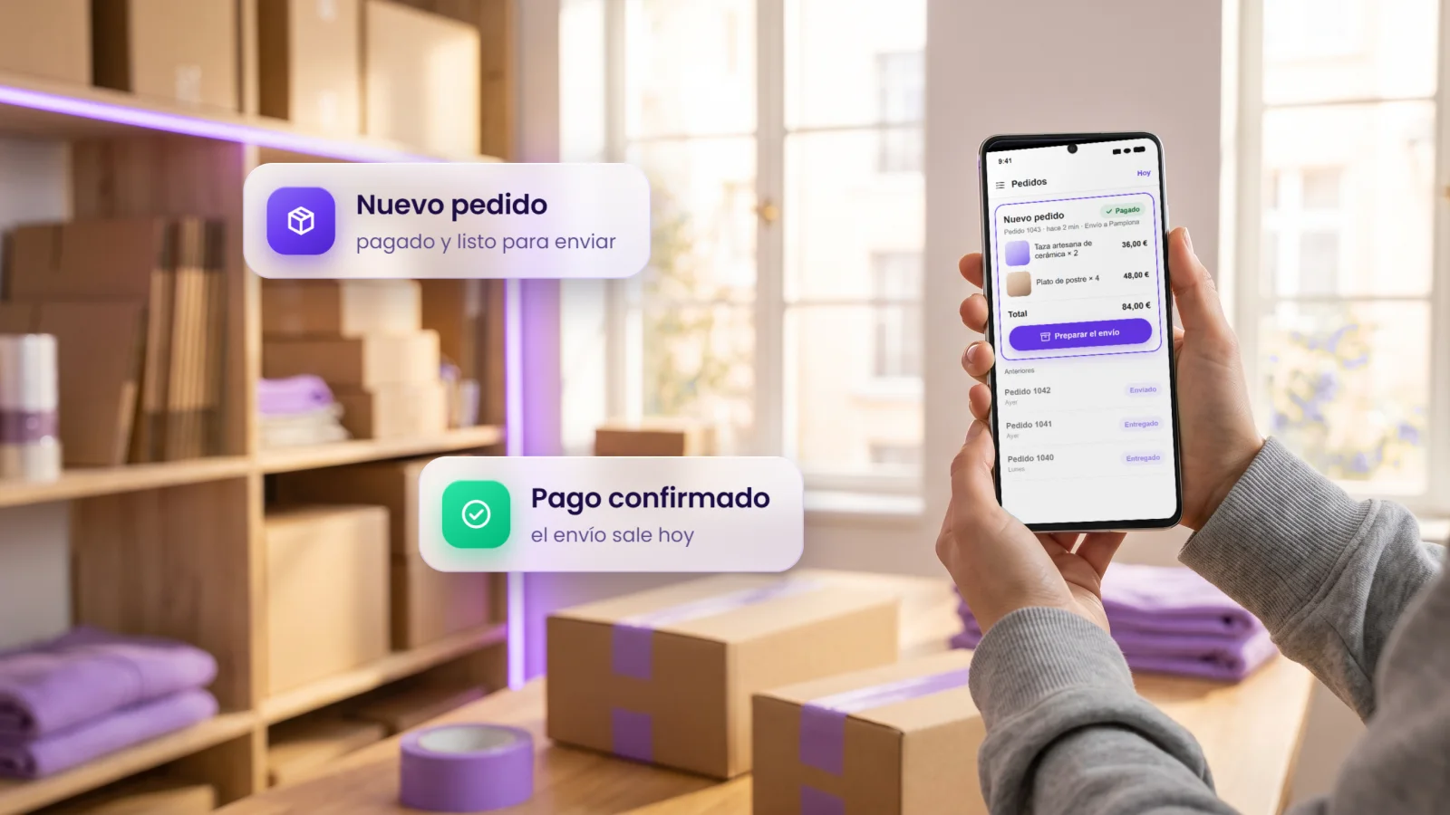 Manos con un móvil que enseña un pedido nuevo pagado y listo para enviar, en un almacén con cajas y cinta violeta